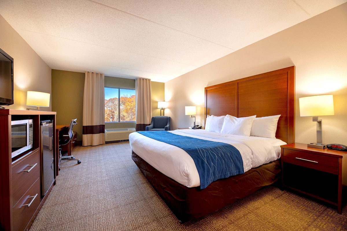 A hotel room with a large bed, a desk with a chair, a TV, and a window with curtains.