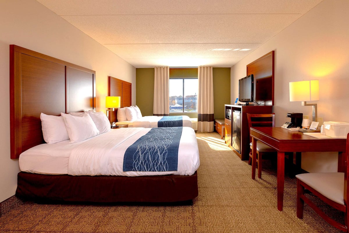 A hotel room with two beds, a desk, a television, and a window with curtains.