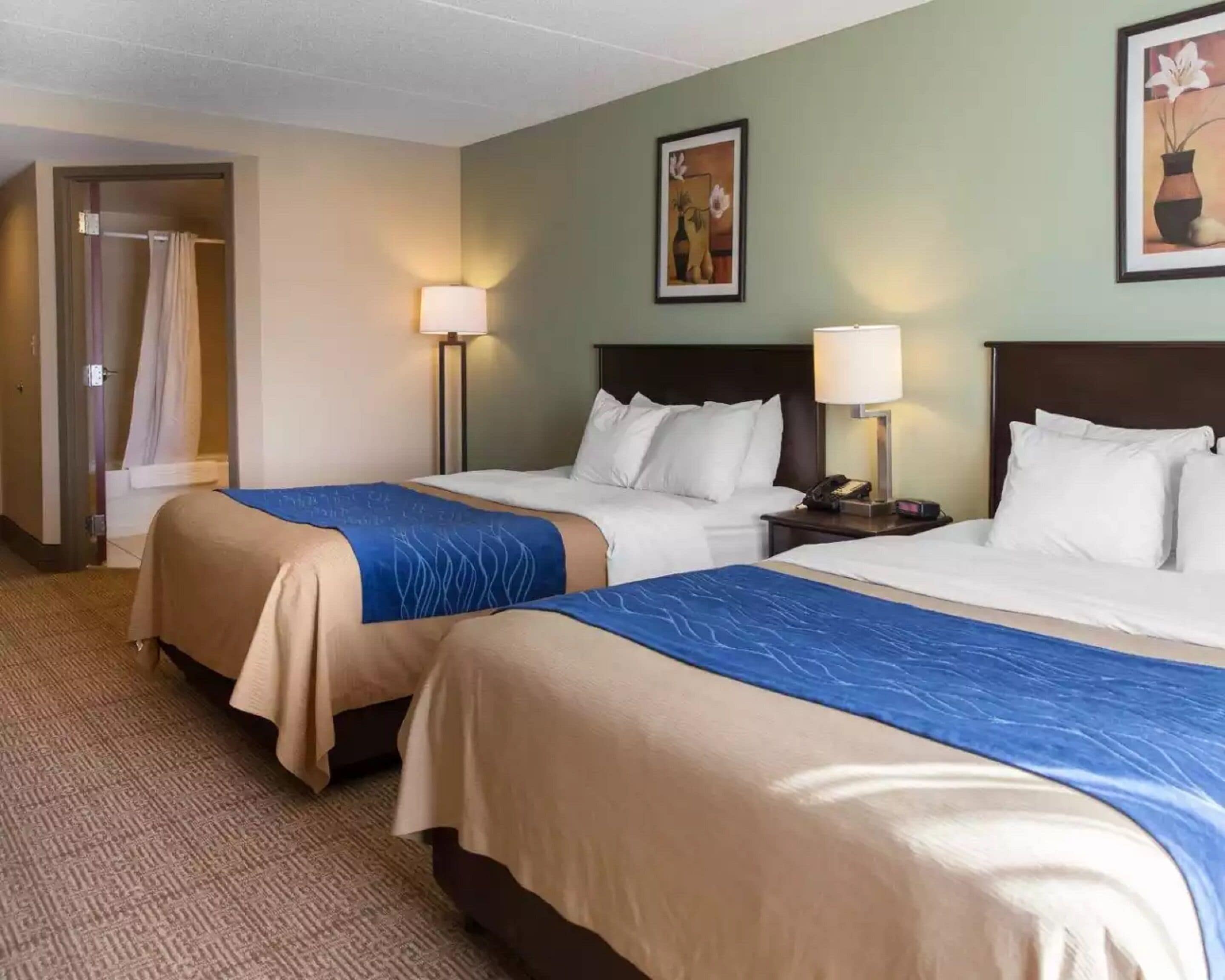 A hotel room with two beds, a bathroom, and a nightstand with a lamp.