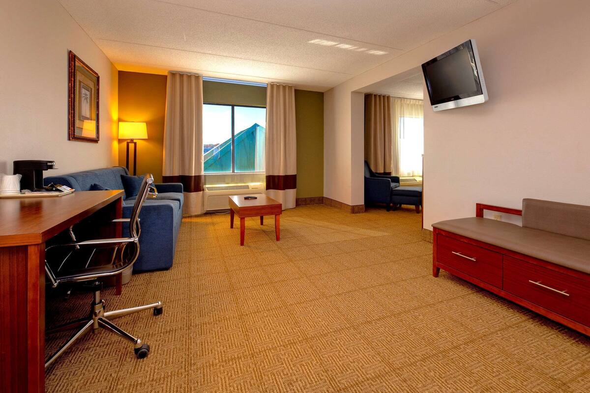 A hotel room with a desk, chair, sofa, TV, and a view of a mountain.