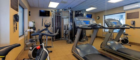 Un gimnasio con equipamiento cardiovascular, máquinas de pesas y un dispensador de agua.