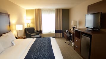 Ett hotellrum med en stor säng, ett skrivbord, en tv och en stol.