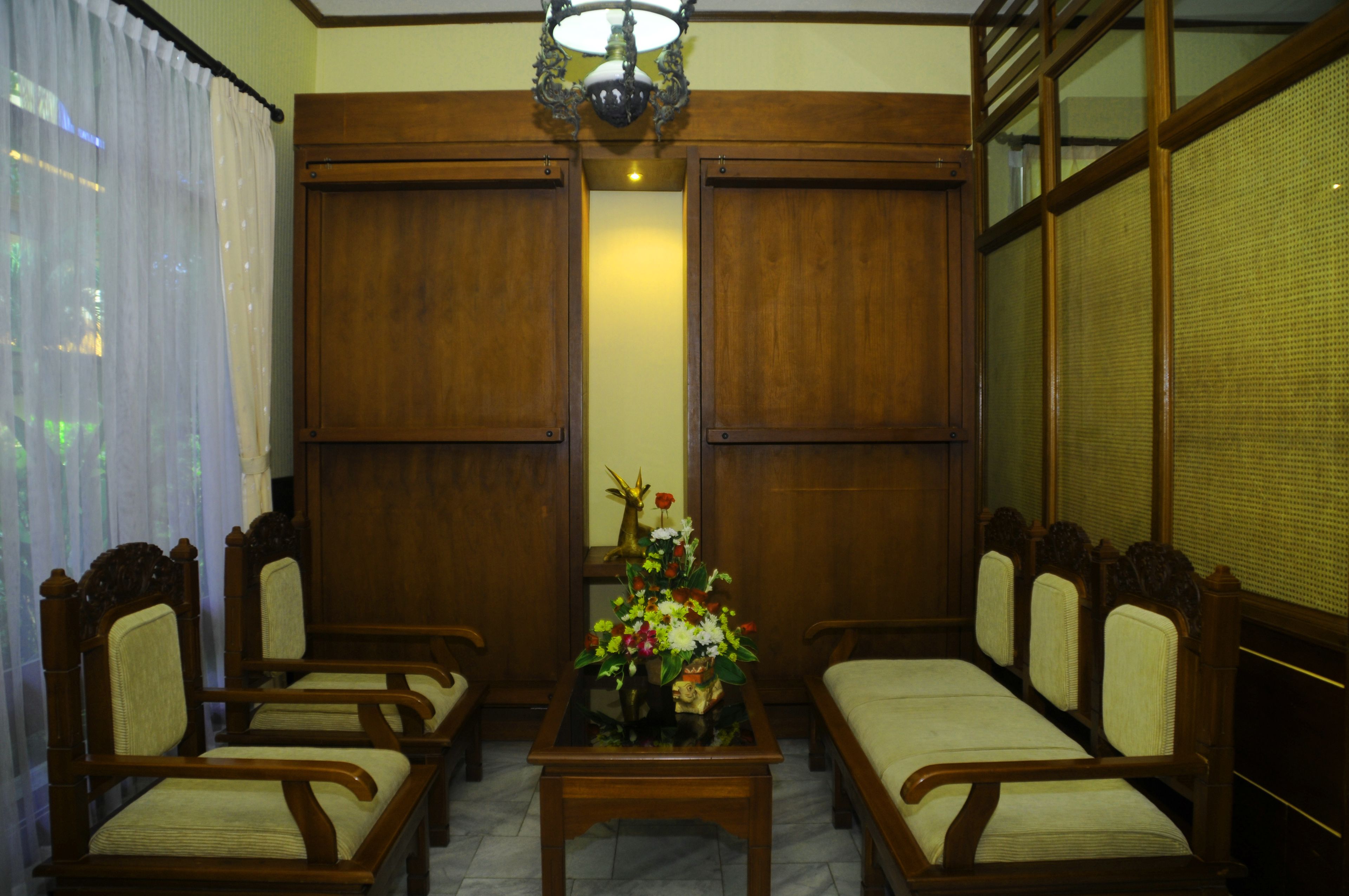 A room with a wooden sofa set, a small table with a floral arrangement, and a large window with a view.