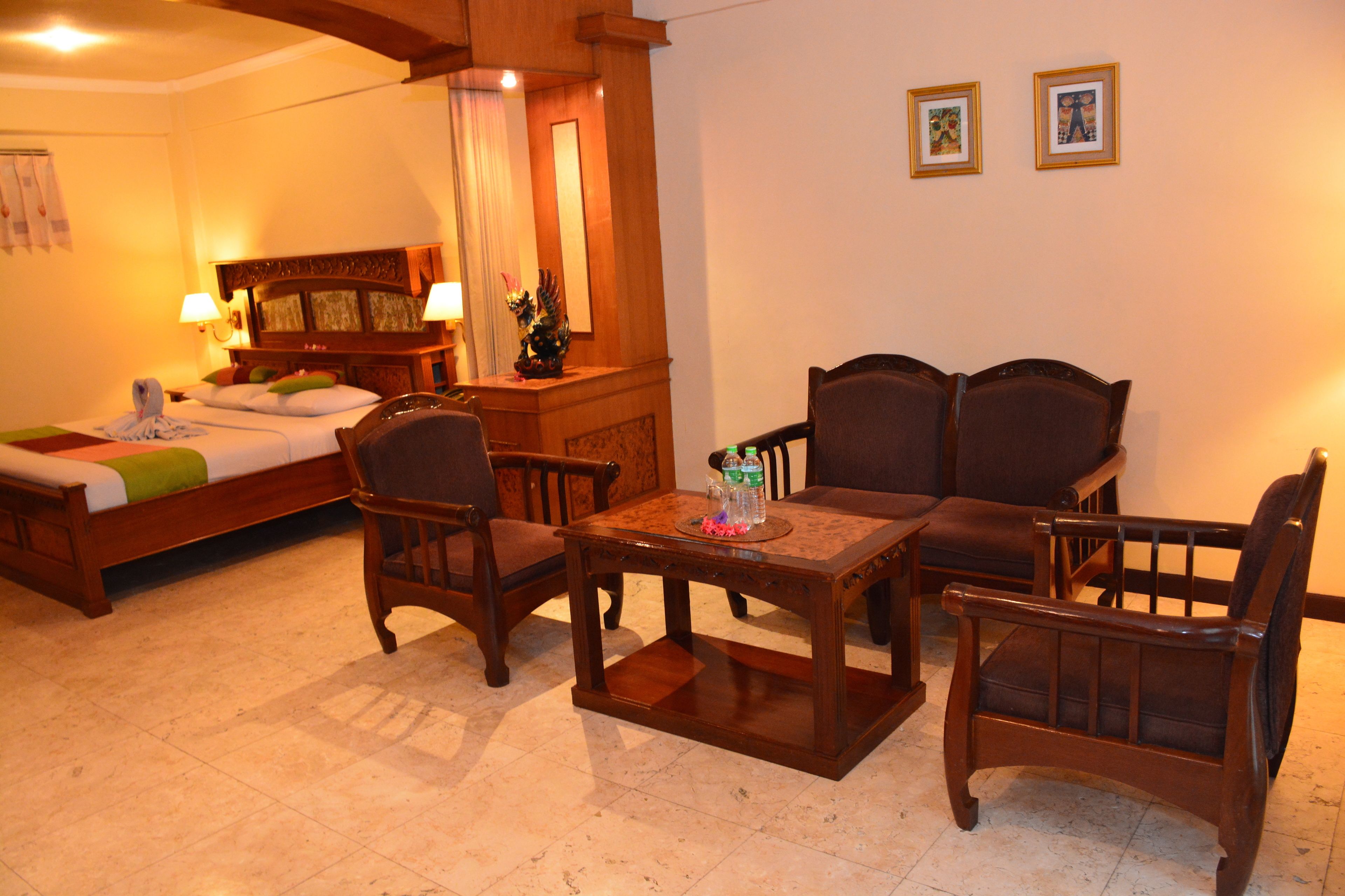 A hotel room with a bed, two armchairs, a wooden table, a nightstand, and a mirror.