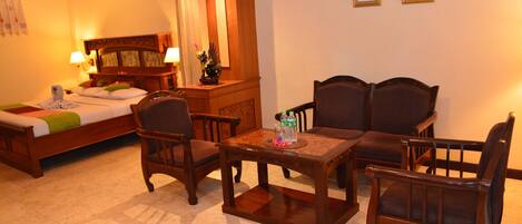 A hotel room with a bed, two armchairs, a wooden table, a nightstand, and a mirror.