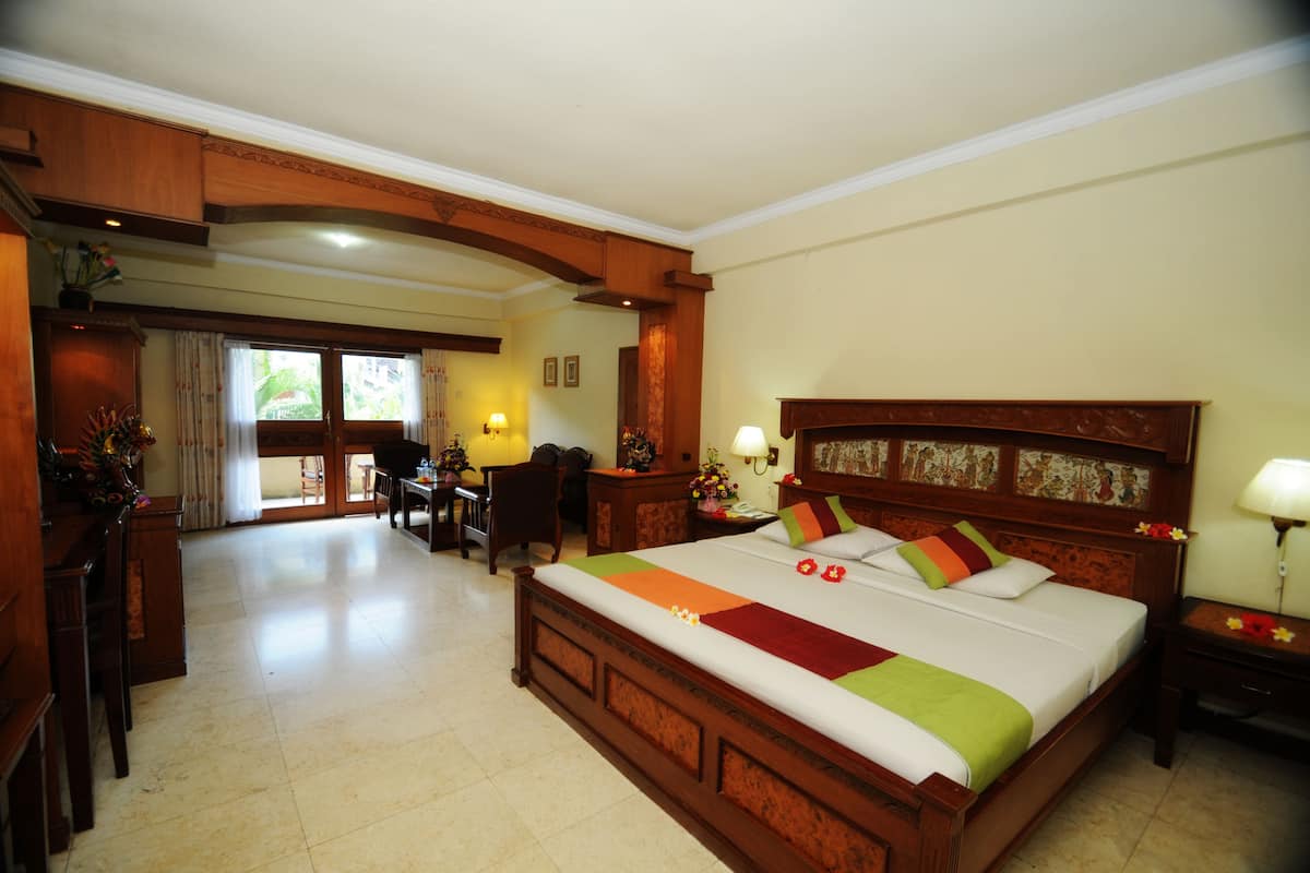 Une chambre d’hôtel spacieuse, dotée d’un grand lit, d’une tête de lit en bois et d’un coin repas avec une table et des chaises.