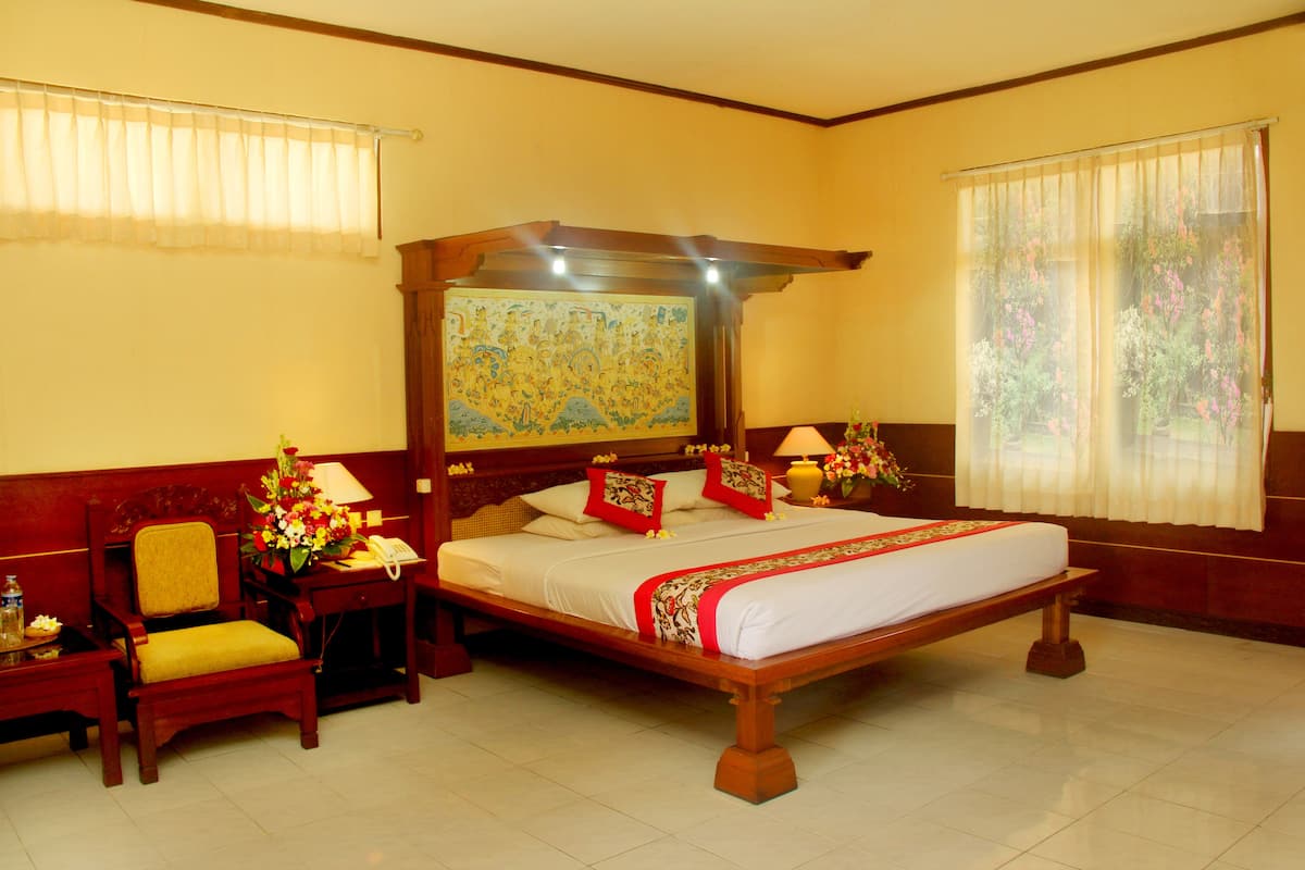 Une chambre d’hôtel avec un grand lit, une tête de lit en bois, deux tables de chevet avec des lampes, une chaise et une fenêtre avec des rideaux légers.