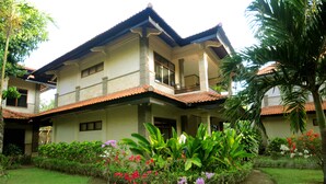 A two-story house with a balcony, surrounded by lush greenery and flowering plants. - Melasti Beach Resort & Spa (Legian)