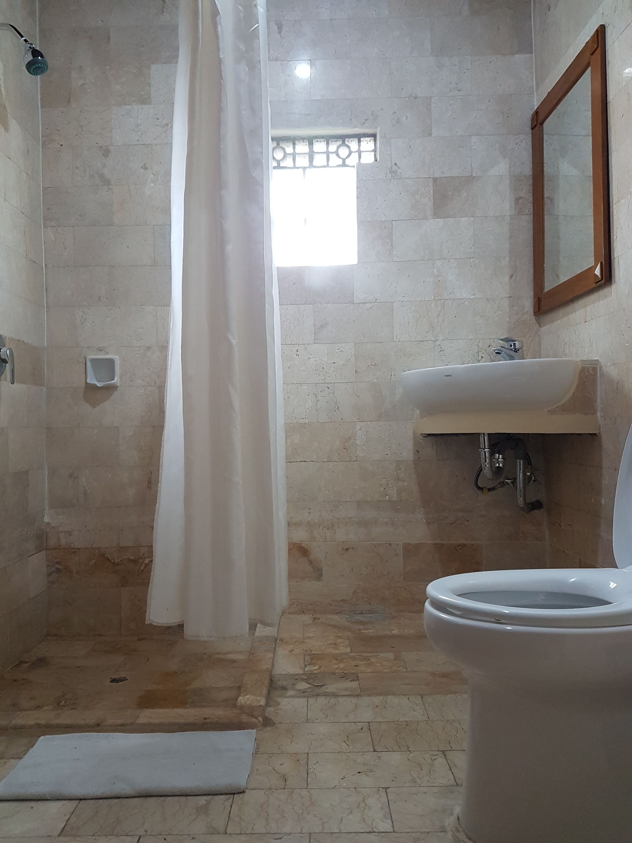 A bathroom with a shower, toilet, sink, and a window with bars.