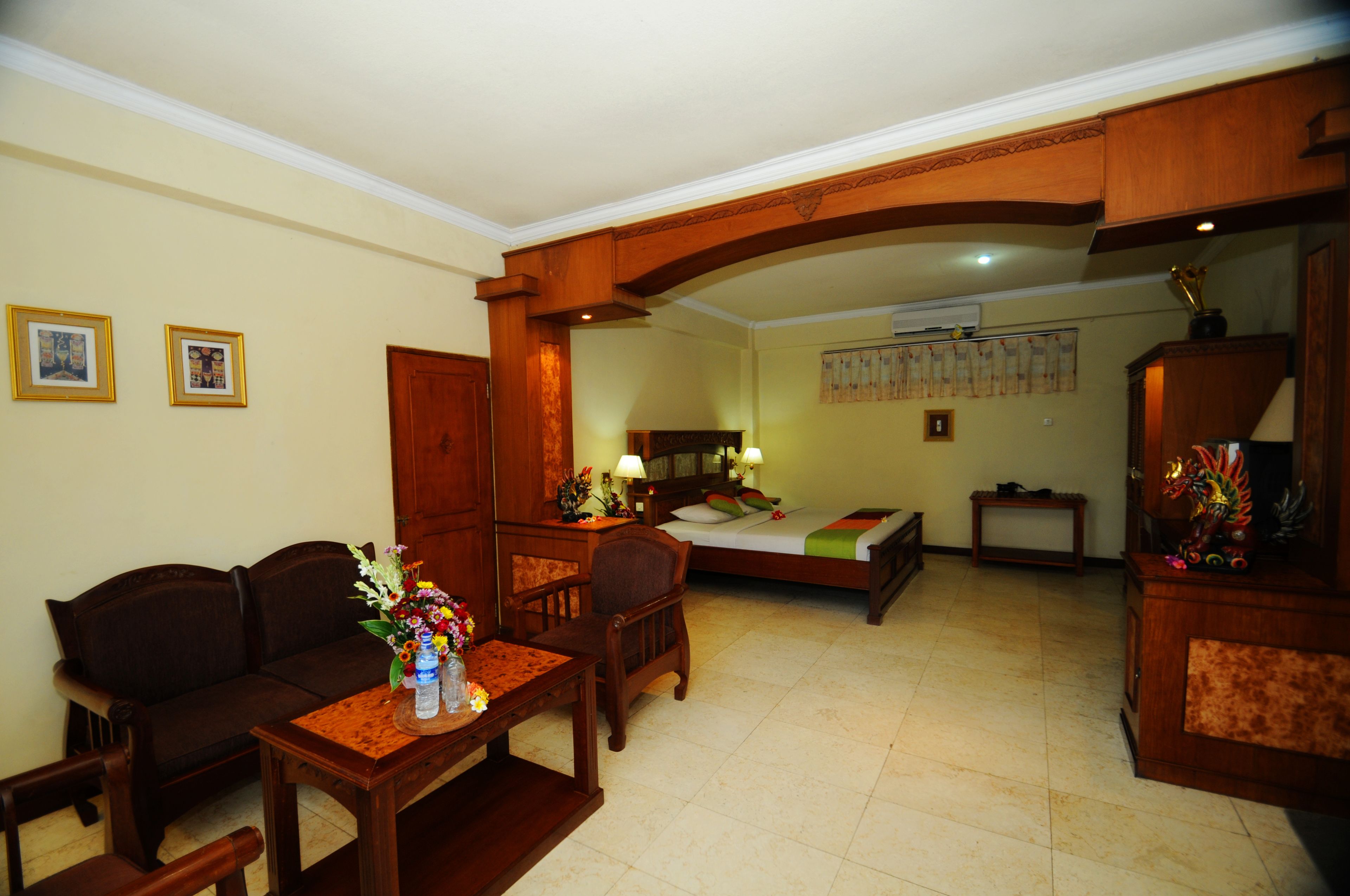 A hotel room with a sofa, a dining table with chairs, a bed, and a wooden cabinet.