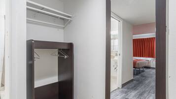 A hotel room with a dark wood vanity, a mirror, and a view of a bed with red curtains.
