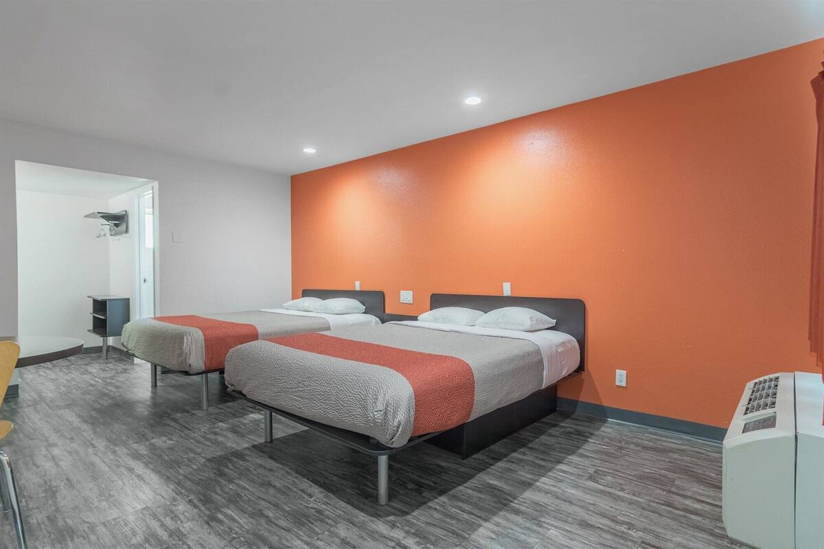 A hotel room with two beds, a grey and orange wall, and a grey floor.