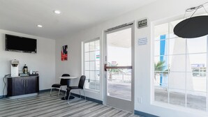 A hotel lobby with a coffee machine, two chairs, a TV, and a large window with a view of the outside. - Motel 6 Barstow, CA - Route 66 (Barstow)