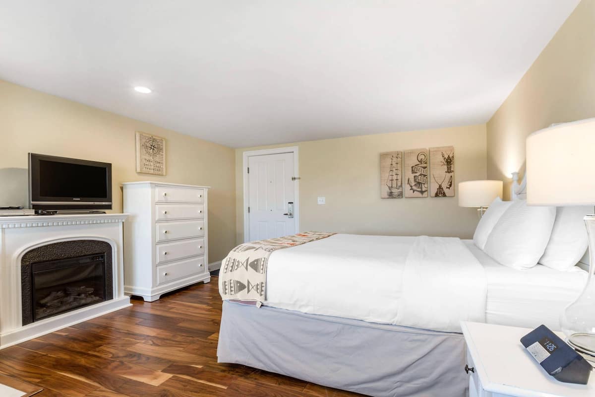 A hotel room with a bed, a television, a fireplace, a dresser, and artwork on the walls.