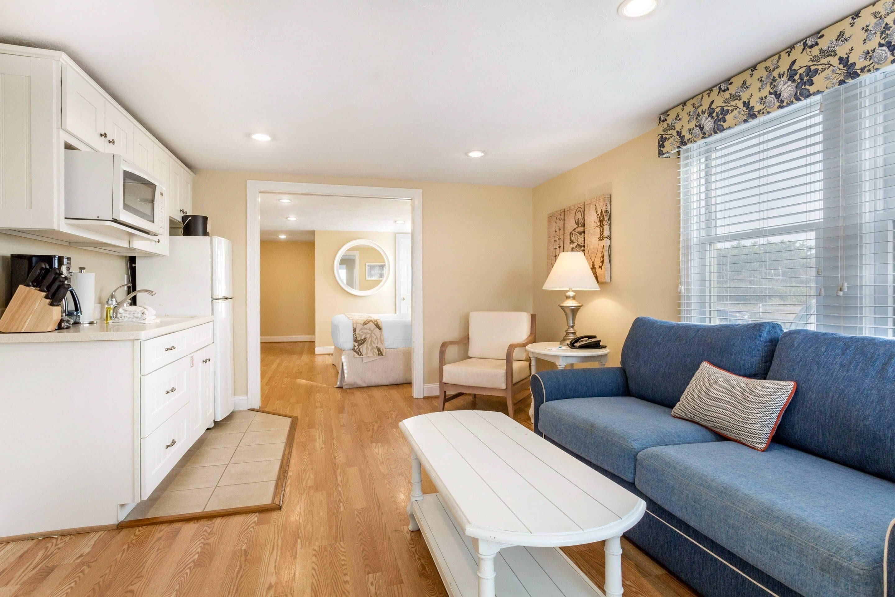 A compact living space with a kitchenette, a sofa, a small table, and a lamp.