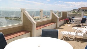 A beachside patio with a table and chairs, a glass balustrade, and a view of the ocean and beach. - Bluegreen Vacations The Breakers Resort, an Ascend Collection Resort (Dennis Port)