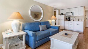 A living room with a blue sofa, two side tables with lamps, a coffee table, and a kitchen area with white cabinets and appliances. - Bluegreen Vacations The Breakers Resort, an Ascend Collection Resort (Dennis Port)