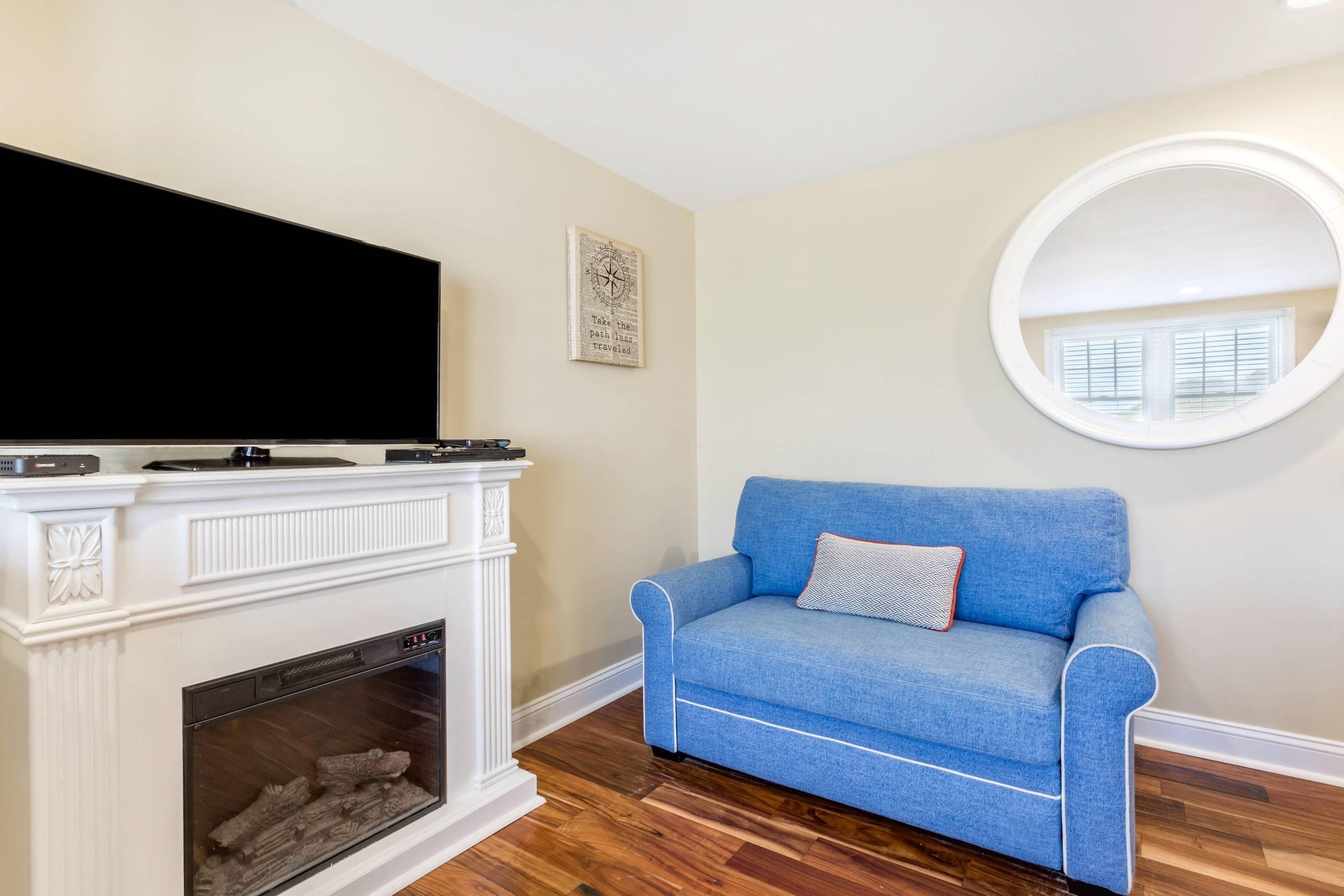 A living room with a fireplace, a blue sofa, a round mirror, and a flat-screen TV.