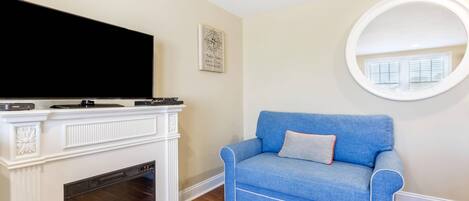 A living room with a fireplace, a blue sofa, a round mirror, and a flat-screen TV.