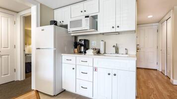 Una cocina con muebles blancos, un microondas integrado y un refrigerador.