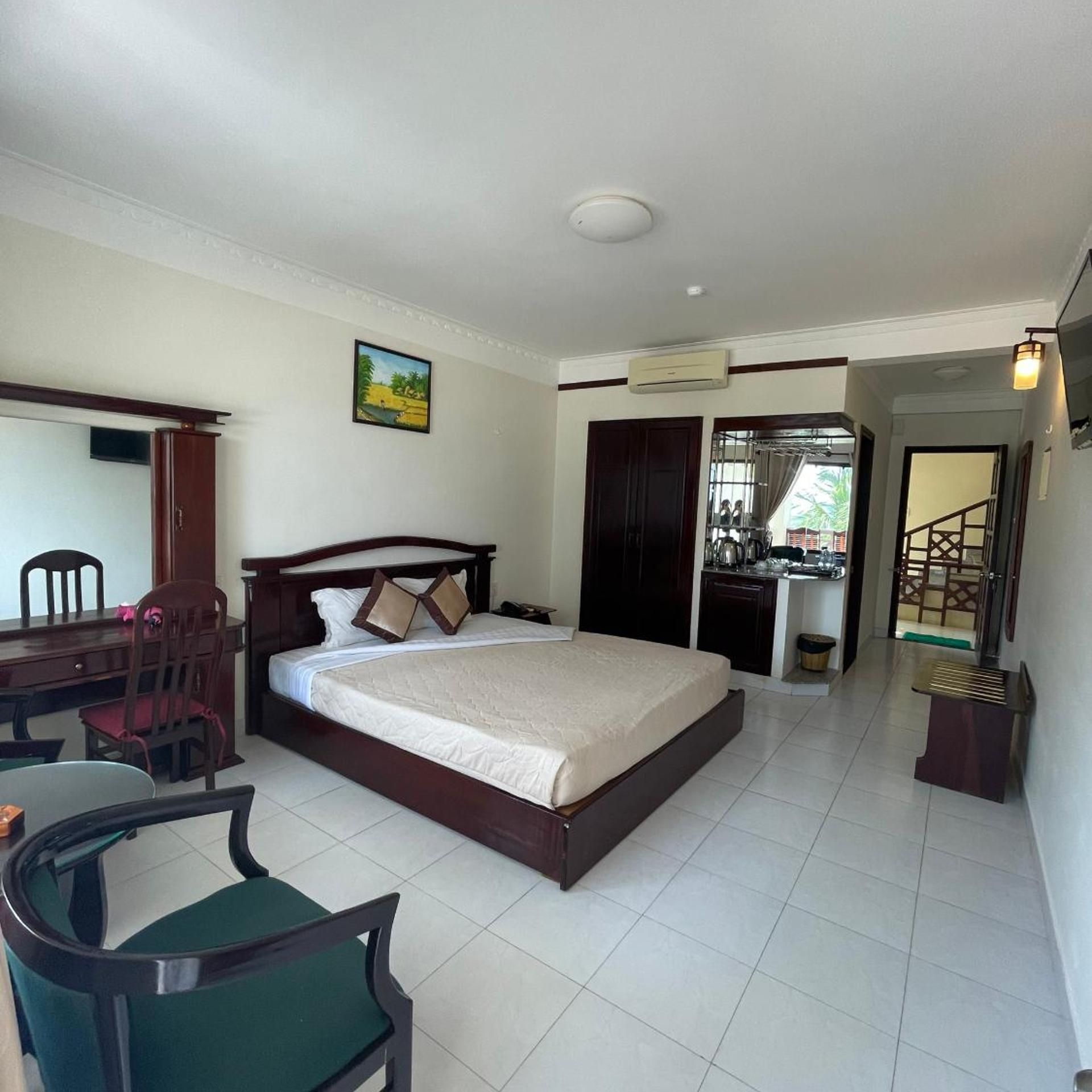 A hotel room with a bed, a desk, a chair, a dining table, and a kitchen area.