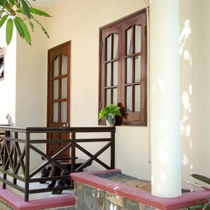 A building facade with two wooden doors and windows, a metal railing, and a potted plant. - Ocean Star Resort (Phan Thiet)