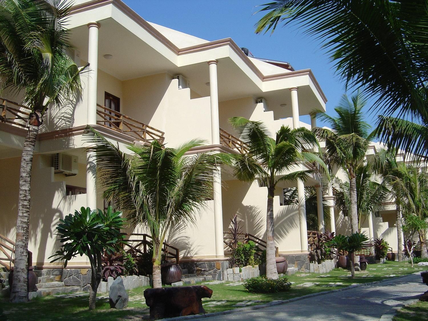 A hotel with multiple floors, palm trees, and a well-maintained lawn.