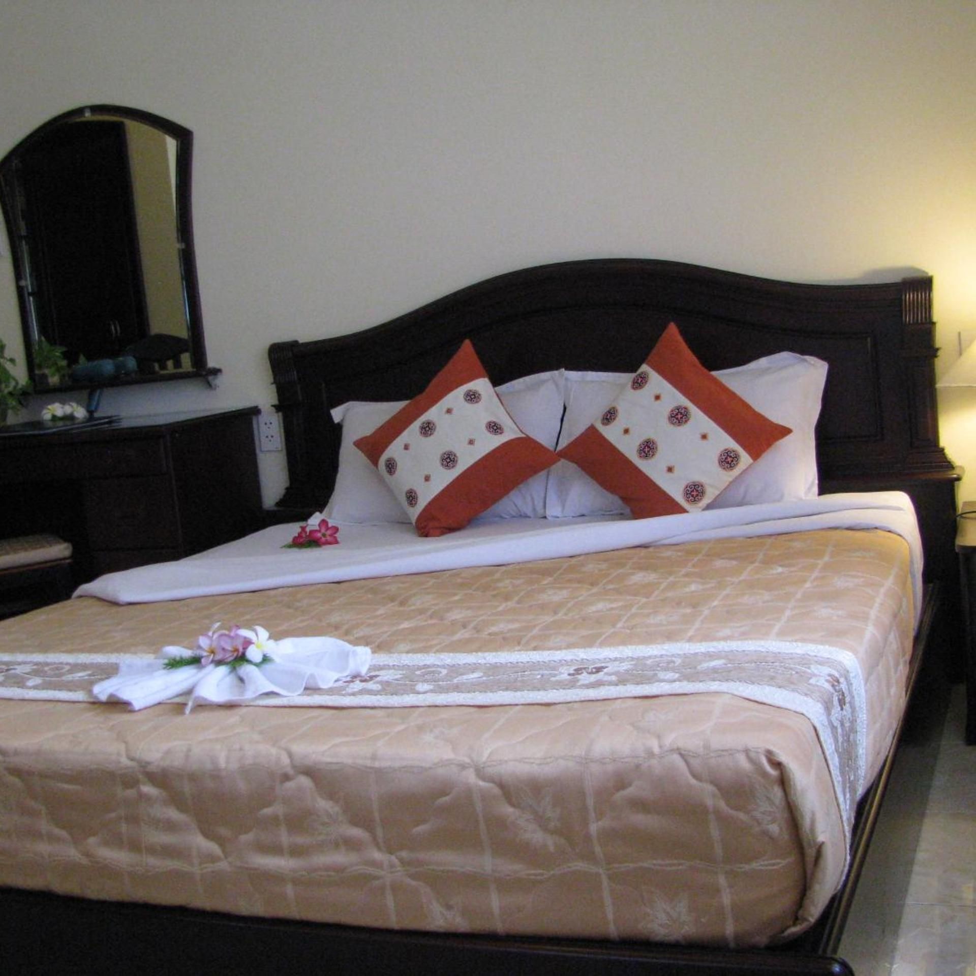 A neatly made bed with a beige bedspread, two pillows with a geometric pattern, and a decorative floral arrangement on the bed.