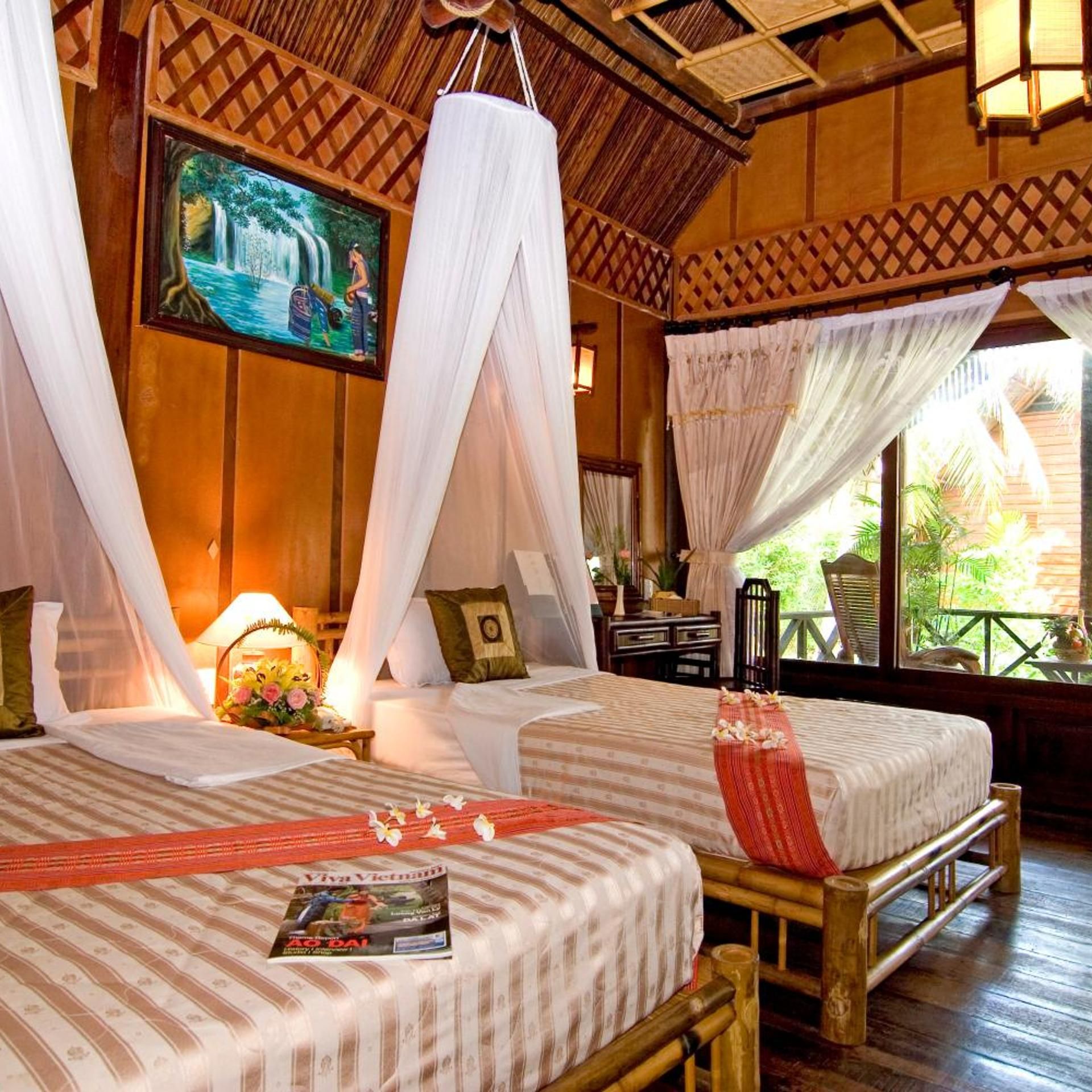 A room with two beds, a painting, and a window with a view of greenery.