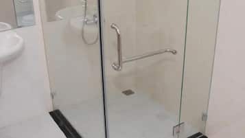 A glass-enclosed shower stall with a handrail, a white sink, and a potted plant on a shelf.