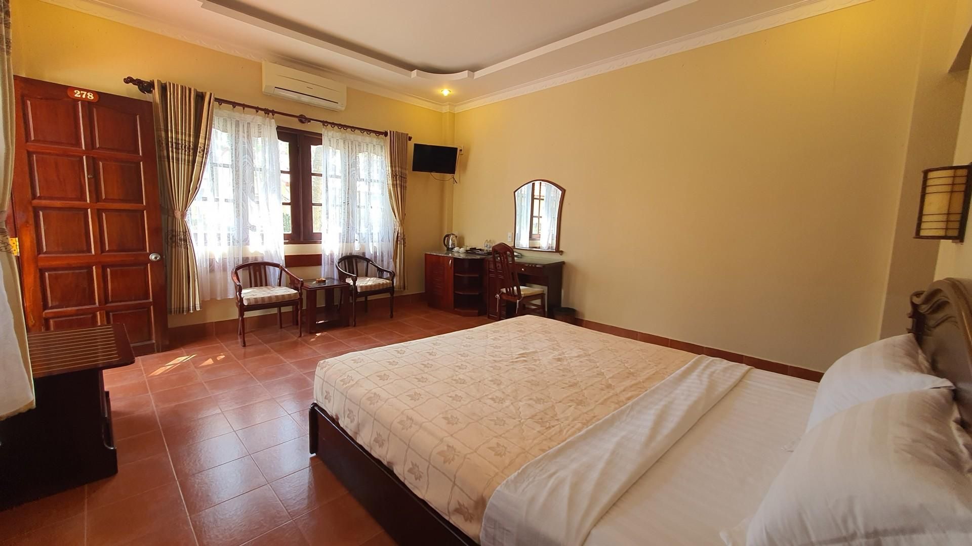 A hotel room with a bed, a desk, two chairs, a television, and a window with curtains.