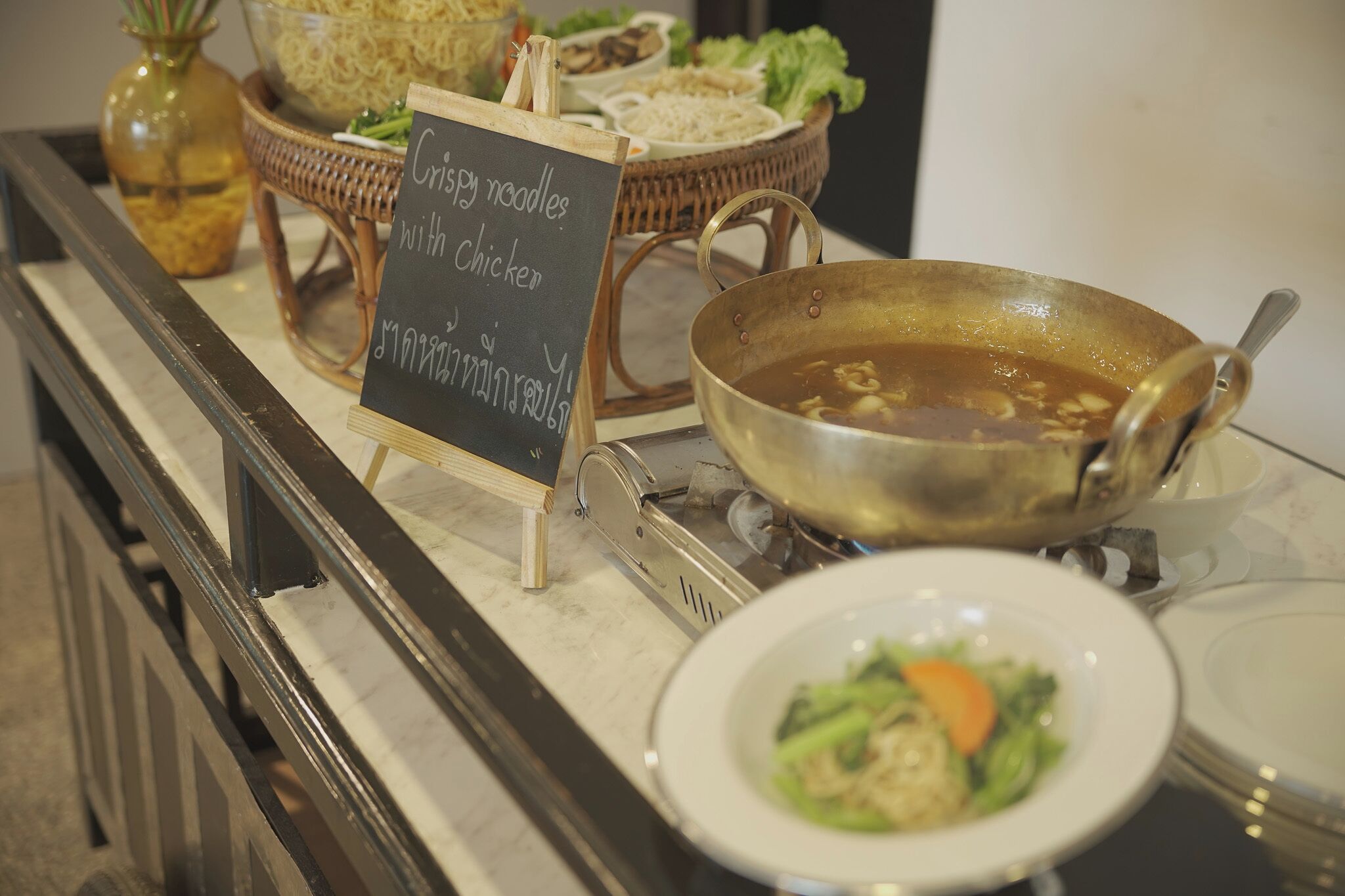 Buffet-pöydässä on kyltti, jossa kerrotaan, että tarjolla on rapeita nuudeleita kanan kanssa, ja erillisessä kulhossa on keittoa.