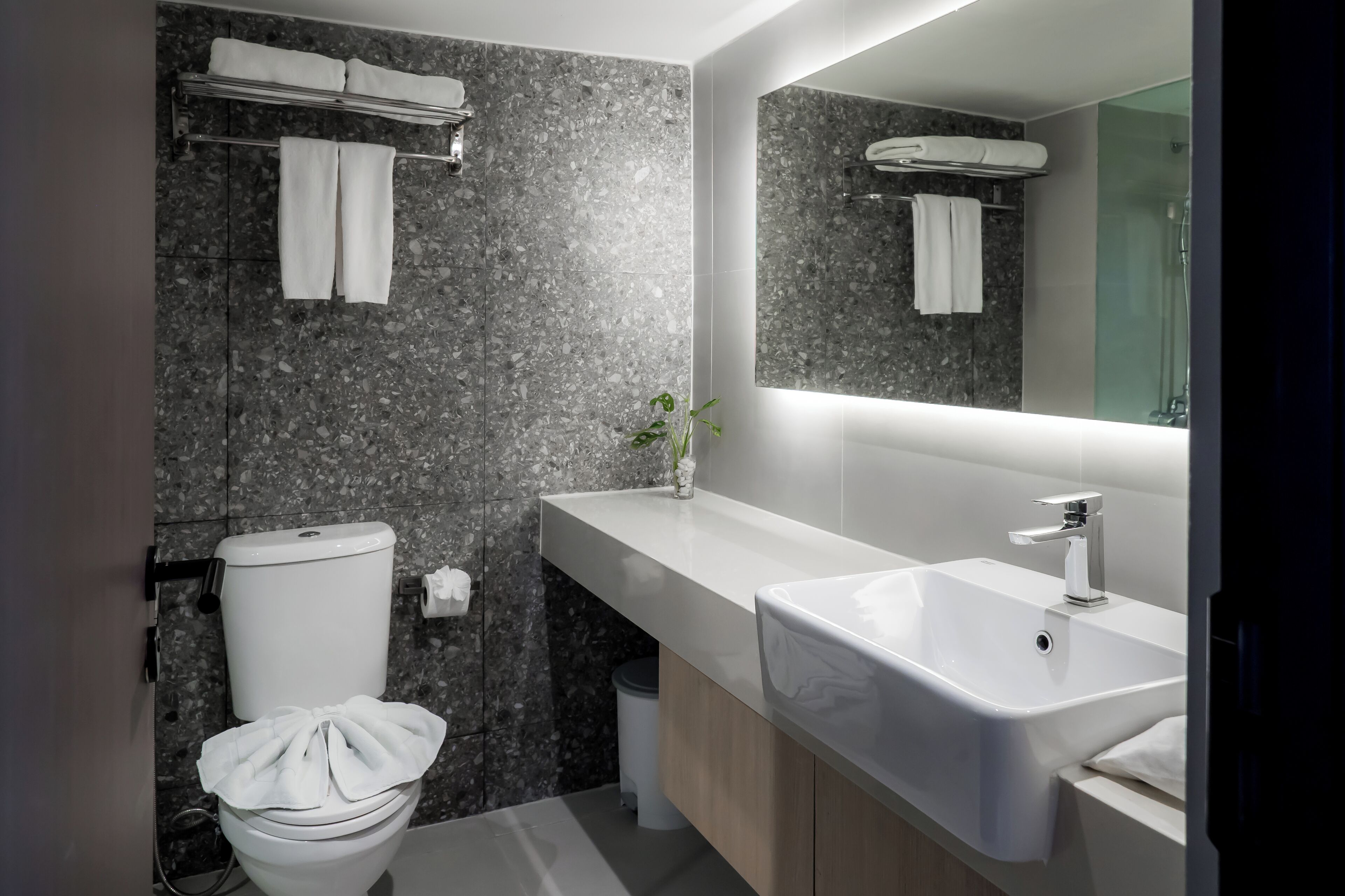 A modern bathroom with a granite backsplash, a white toilet, a sink, and a mirror.