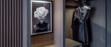 Un baño moderno con una obra de arte enmarcadas de una mujer con una flor, una bata colgada en un perchero y una repisa de madera.