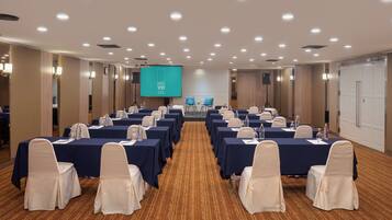 A conference room with tables and chairs, a large screen, and a carpeted floor.