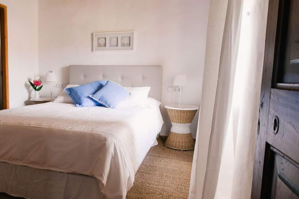 A neatly arranged bedroom with a bed, bedside tables, a mirror, and a framed picture on the wall.