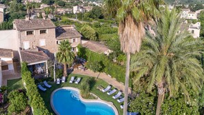 Une piscine entourée de chaises longues, un bâtiment en pierre et des palmiers.
