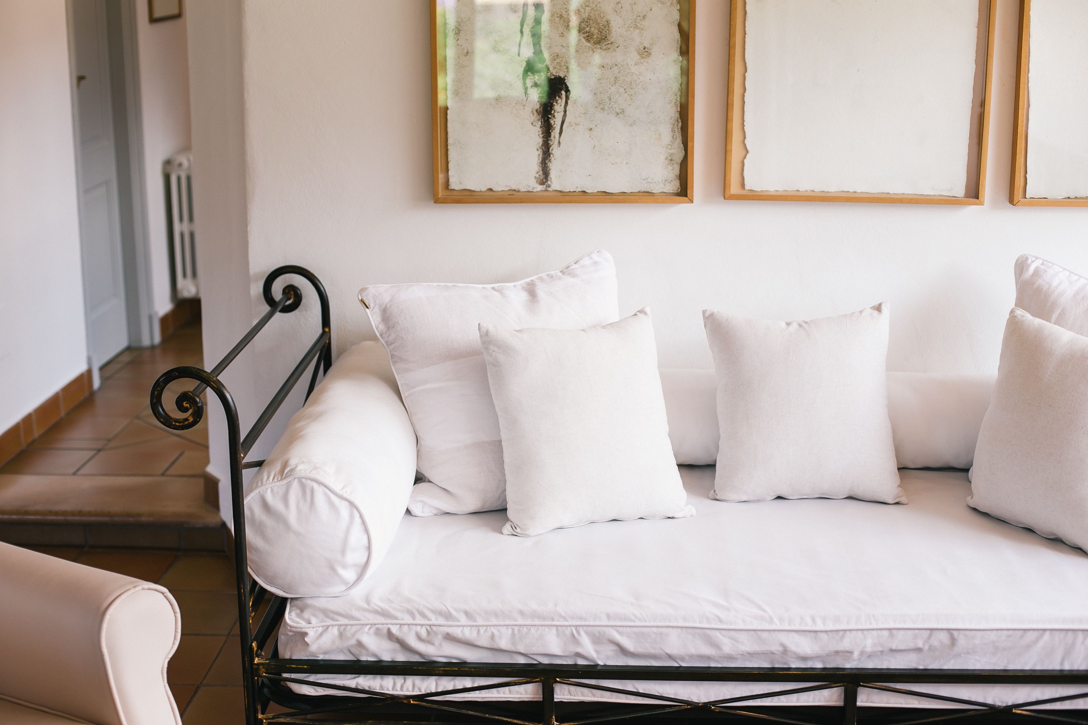 A white sofa with a metal frame and white cushions in a room with a tiled floor and a white wall.