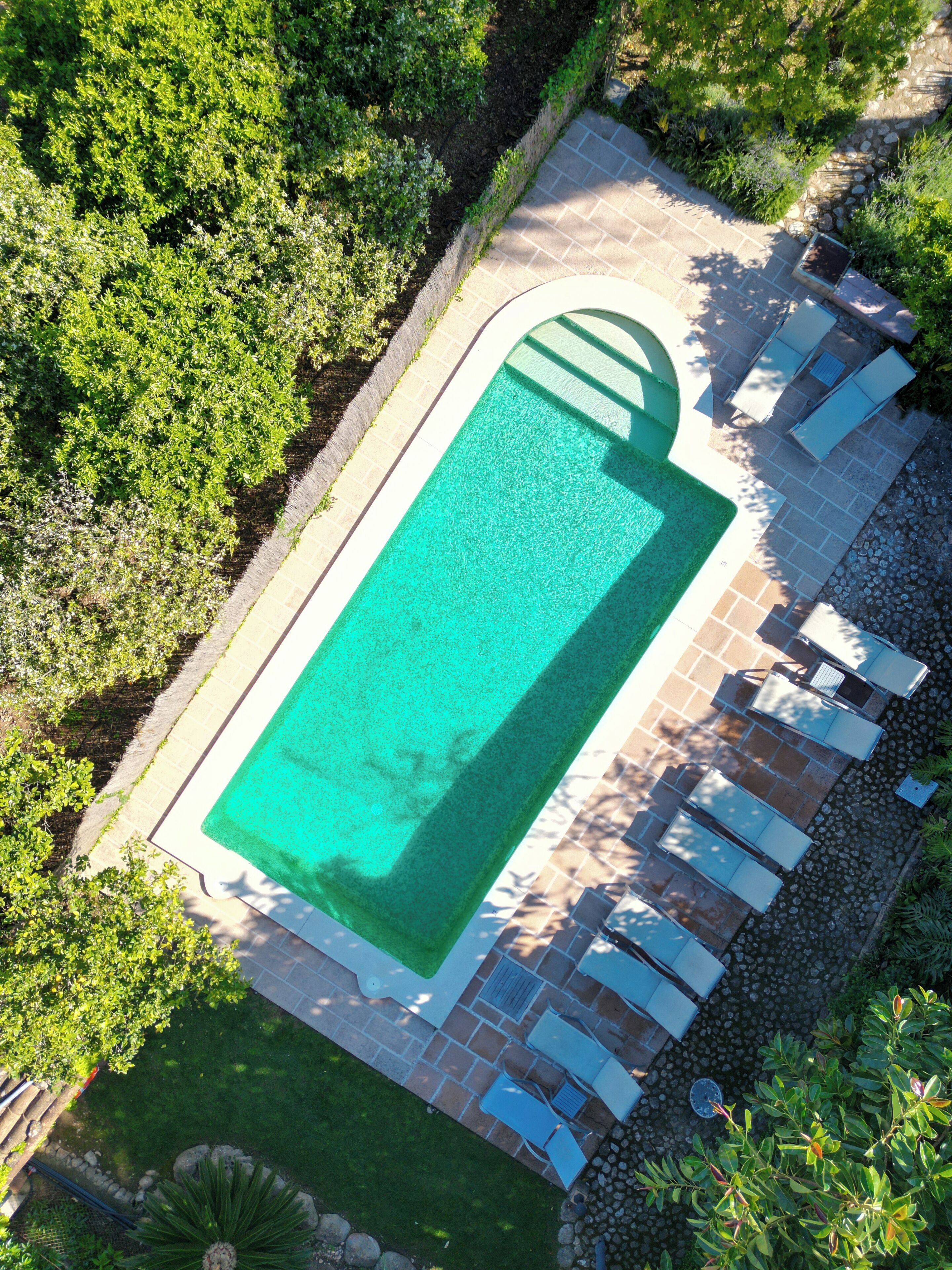 An aerial view of a rectangular swimming pool with a surrounding patio area, including lounge chairs and a small garden.