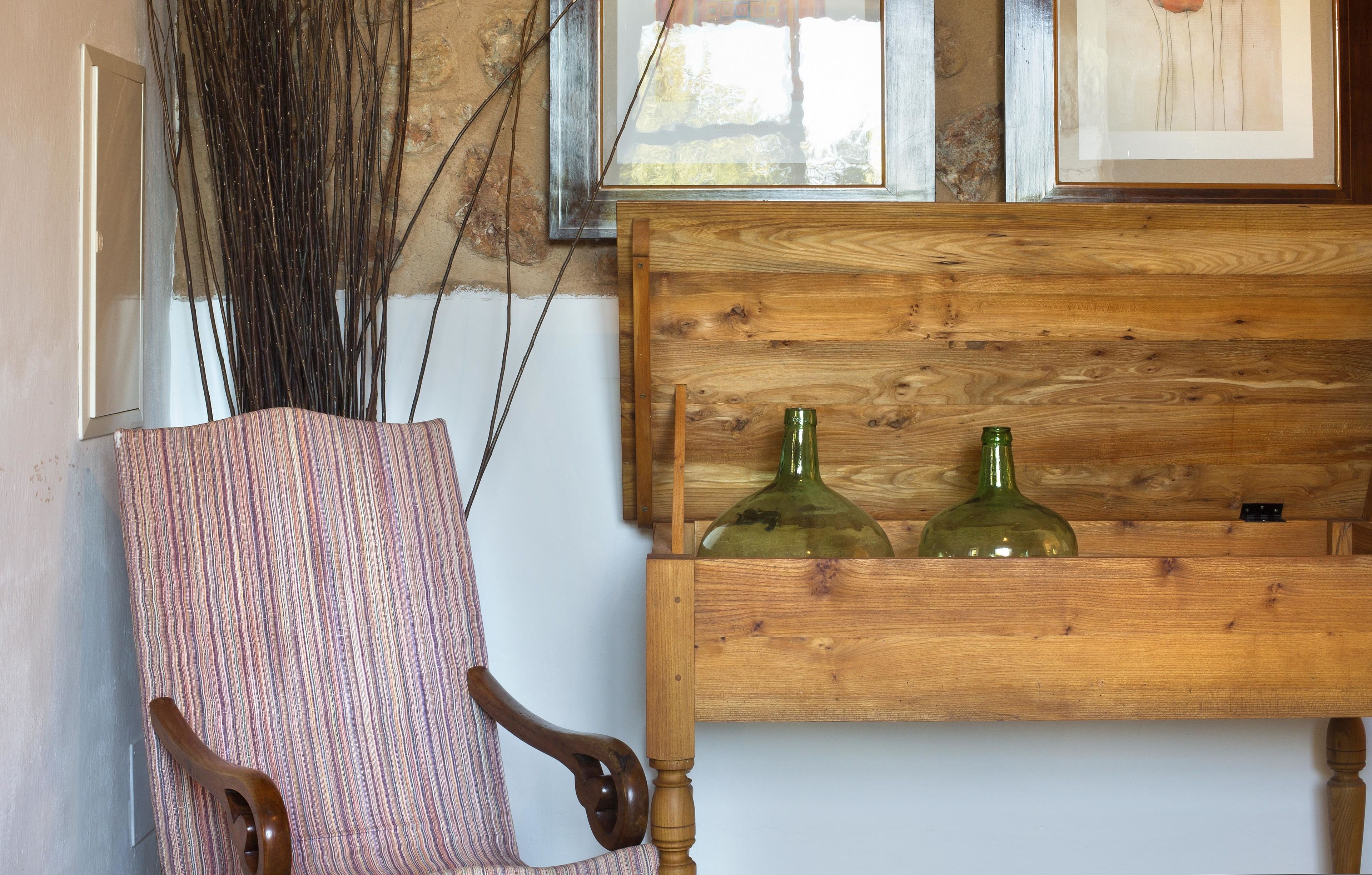A wooden bench with two green bottles, a striped chair, and a window with a view of a stone wall.