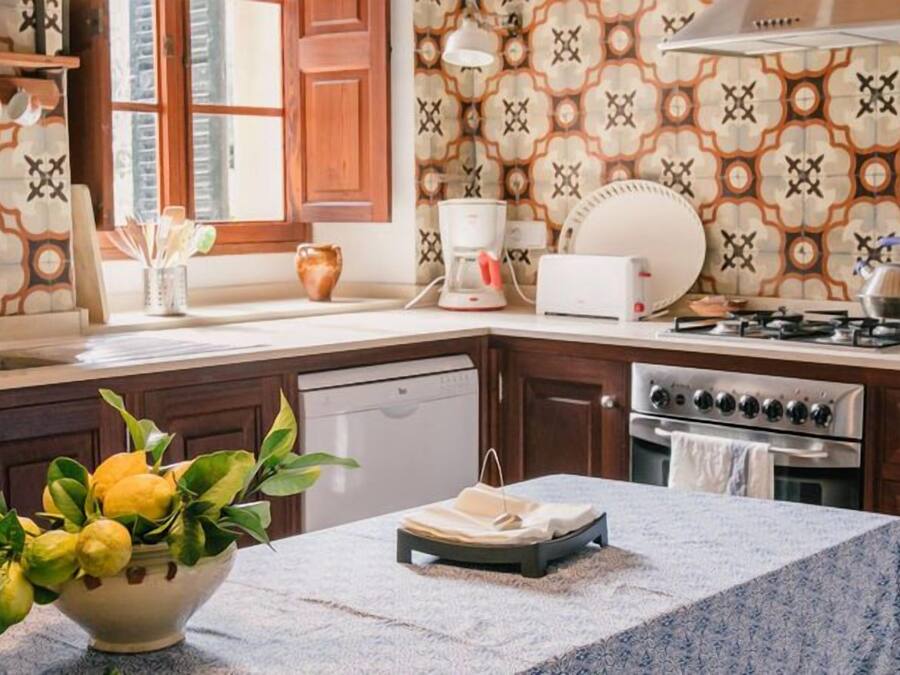 A kitchen with a patterned backsplash, a stove, a sink, and a bowl of lemons on the counter.