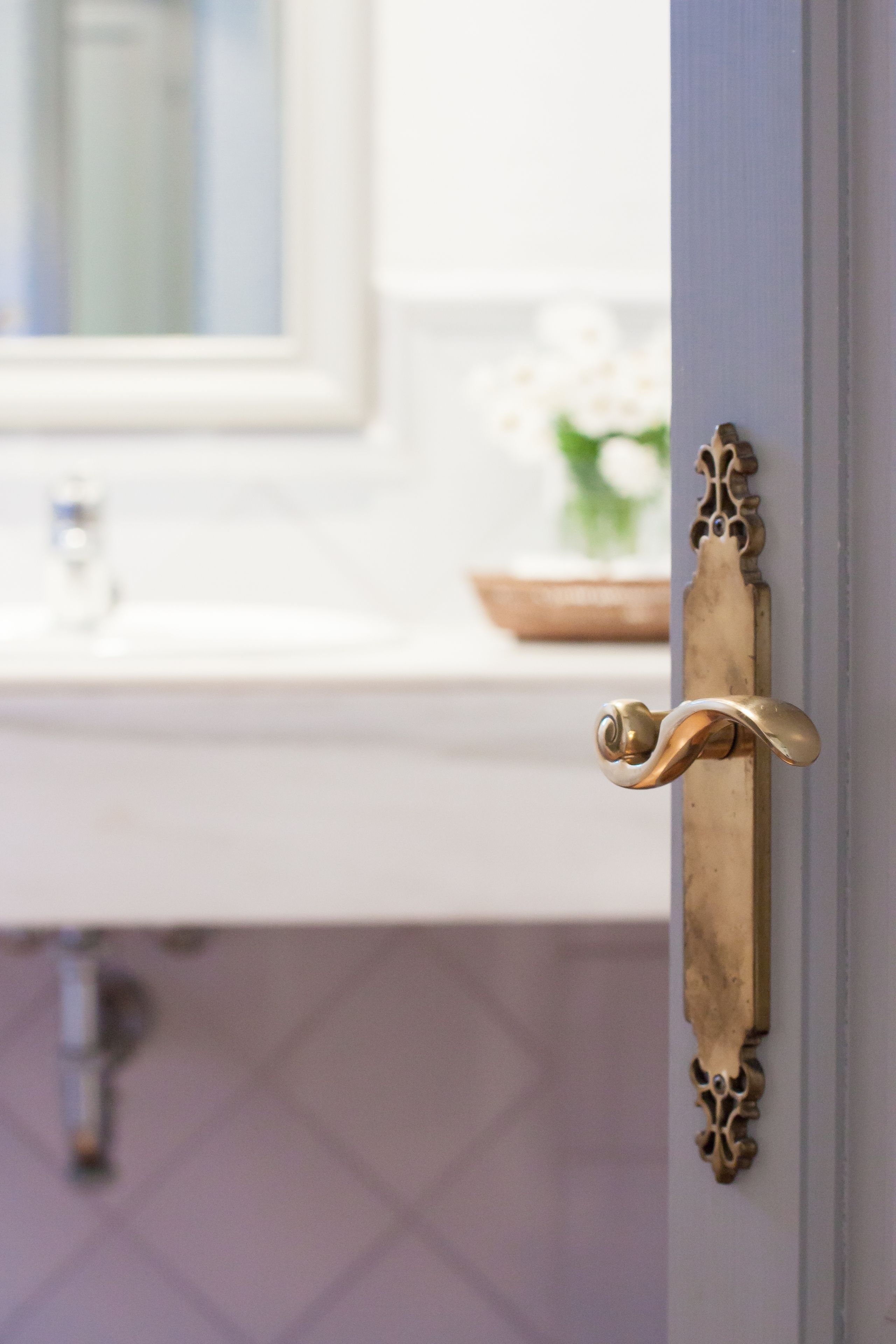 A bathroom with a white sink, a mirror, and a decorative brass door handle.