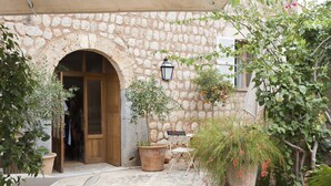 Une cour extérieure avec des murs en pierre, une porte en bois, des plantes en pot et du mobilier d’extérieur.