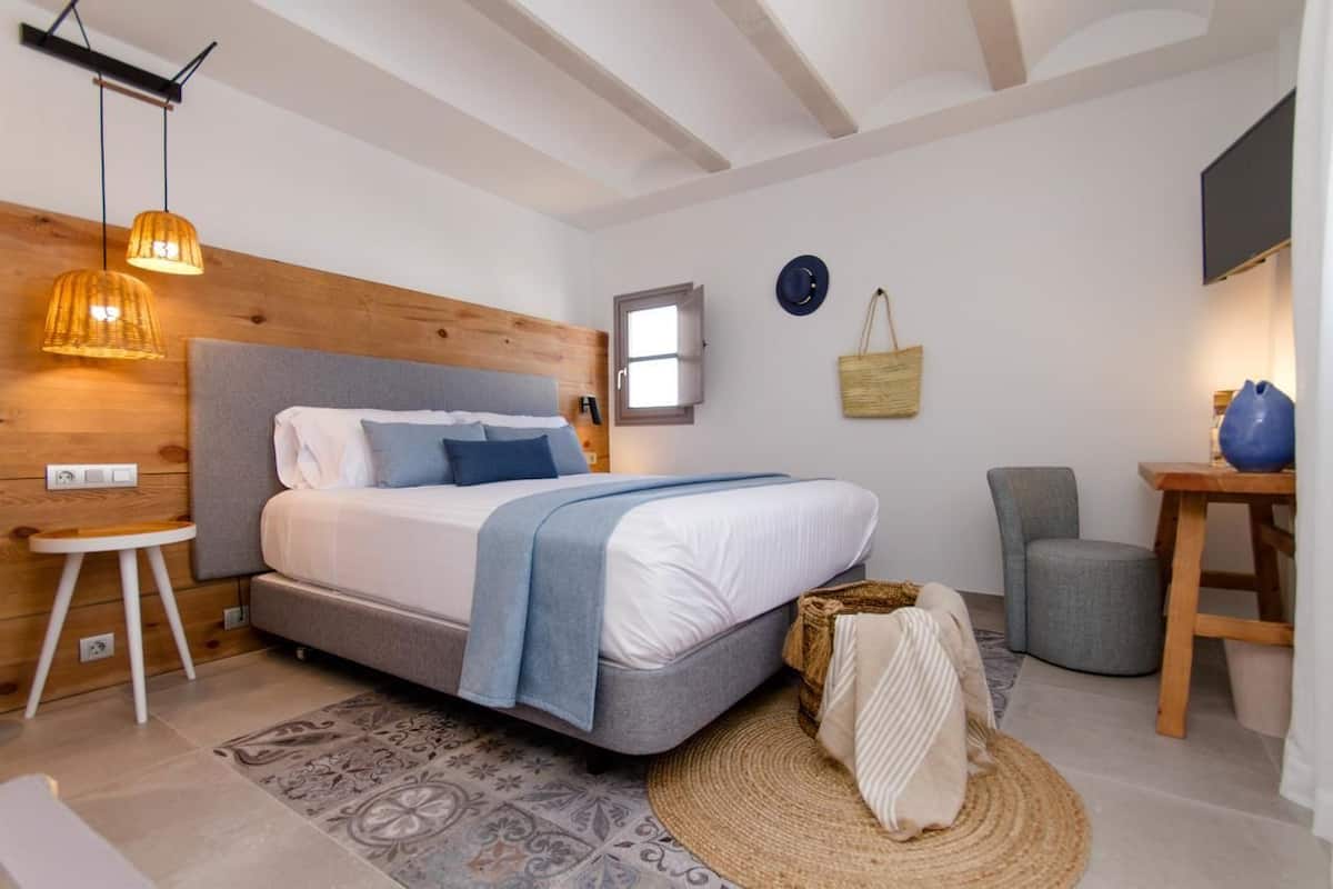 Un dormitorio con cama, mesita de noche, lámpara y ventana.