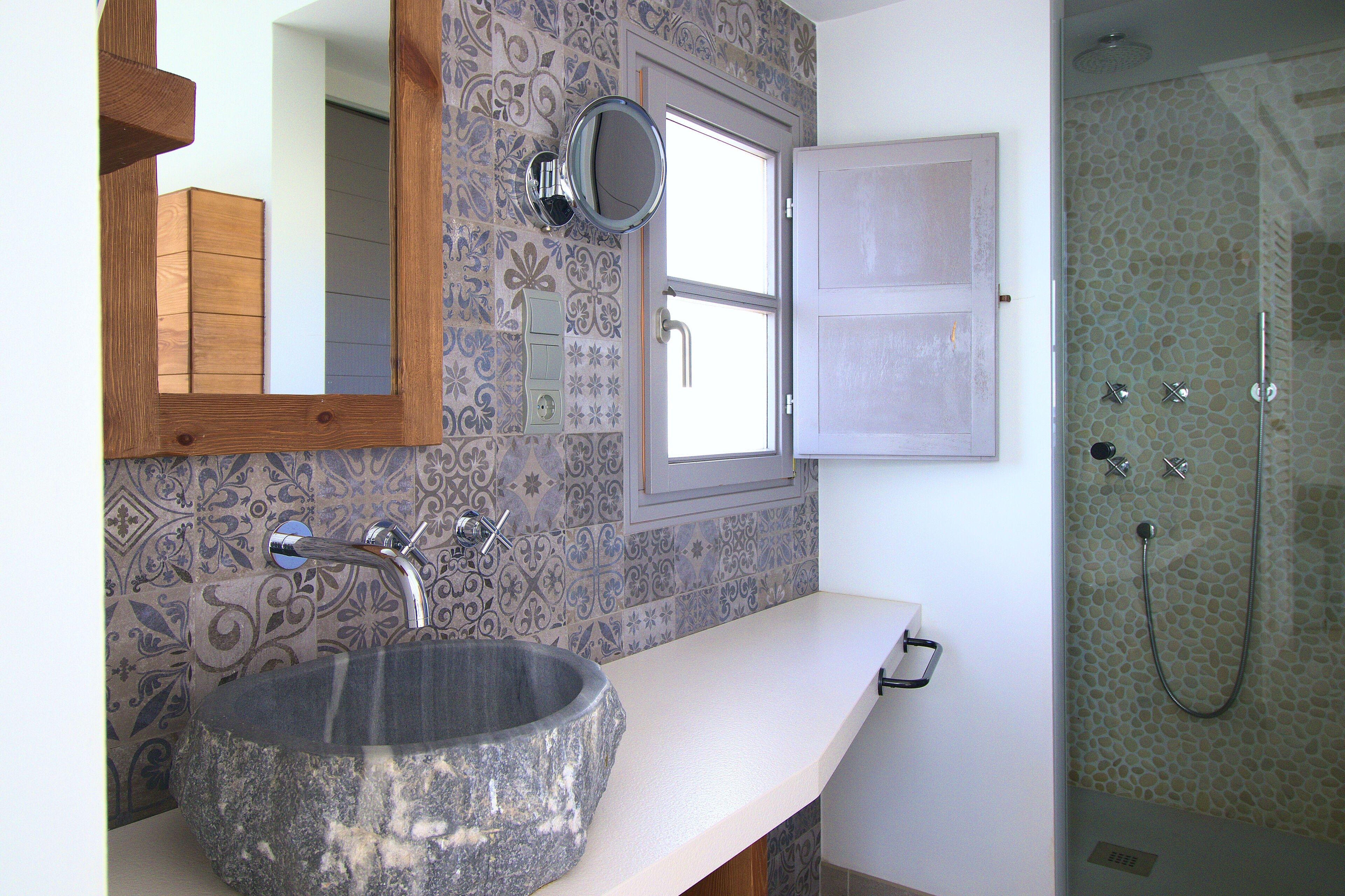 Baño con lavamanos de piedra, espejo, ducha y baldosas con diseño.