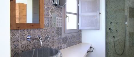 Baño con lavamanos de piedra, espejo, ducha y baldosas con diseño.
