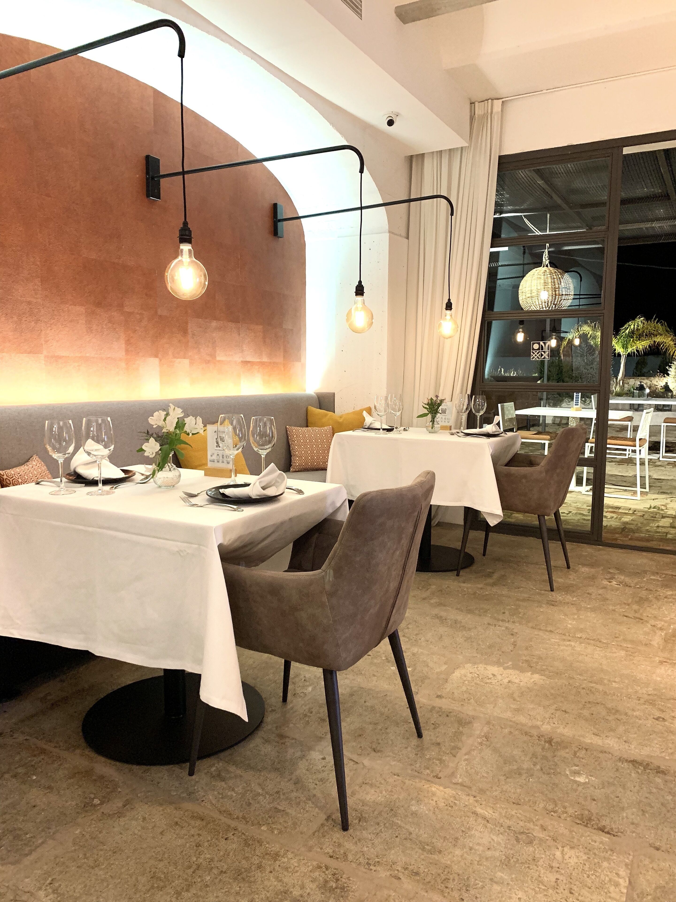 A restaurant with tables set for dining, featuring modern decor and a view of the outdoors.