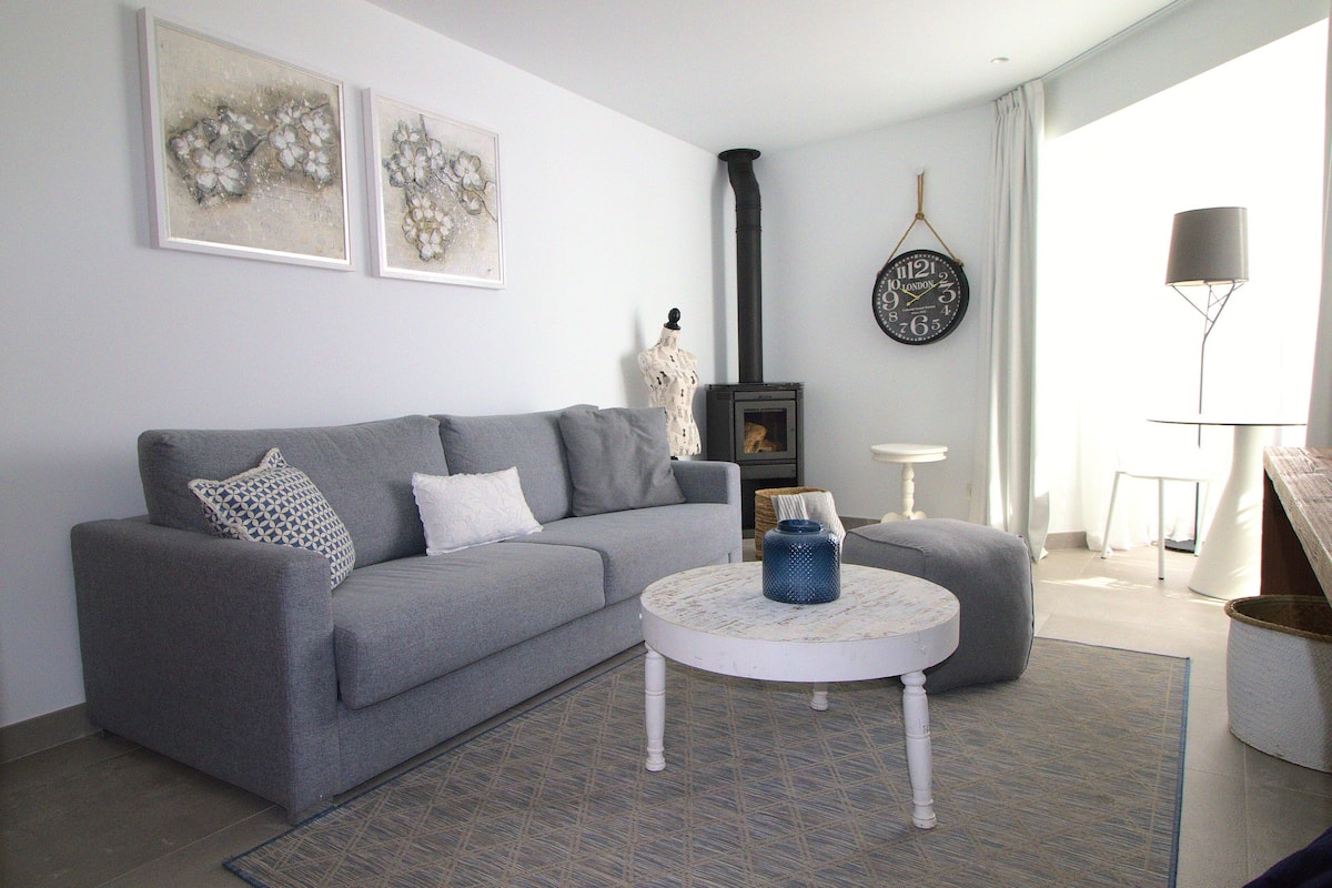 Una sala de estar con un sofá gris, una mesa redonda de centro y un jarrón decorativo.