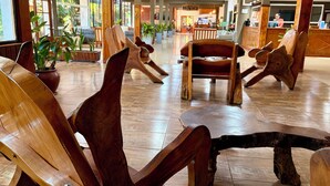 A lobby with wooden chairs and tables, potted plants, and a reception area with a counter.