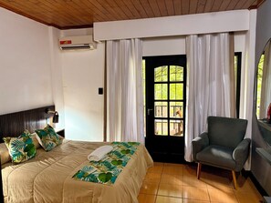 A hotel room with a bed, a chair, a window with curtains, and an air conditioning unit.